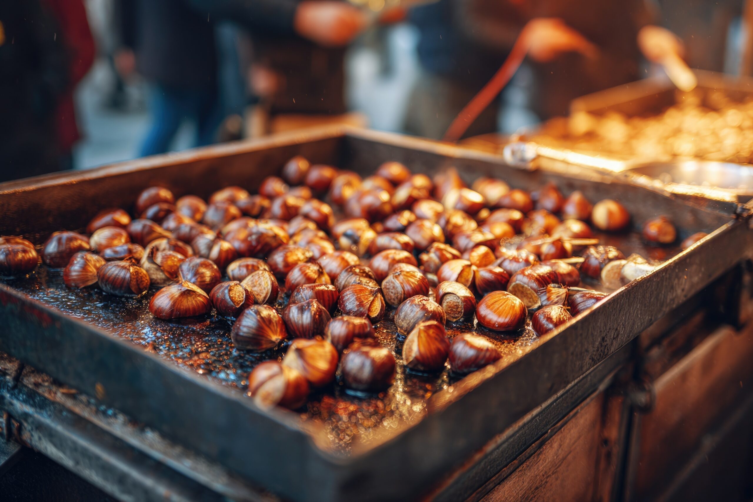 Roasted chestnuts filling a metal vendor pan at an outdoor street market, a direct-to-consumer channel for selling chestnuts